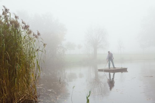 Ausschnitt eines Gartens im Herbst, Mann auf einem Floß auf seinem Teich